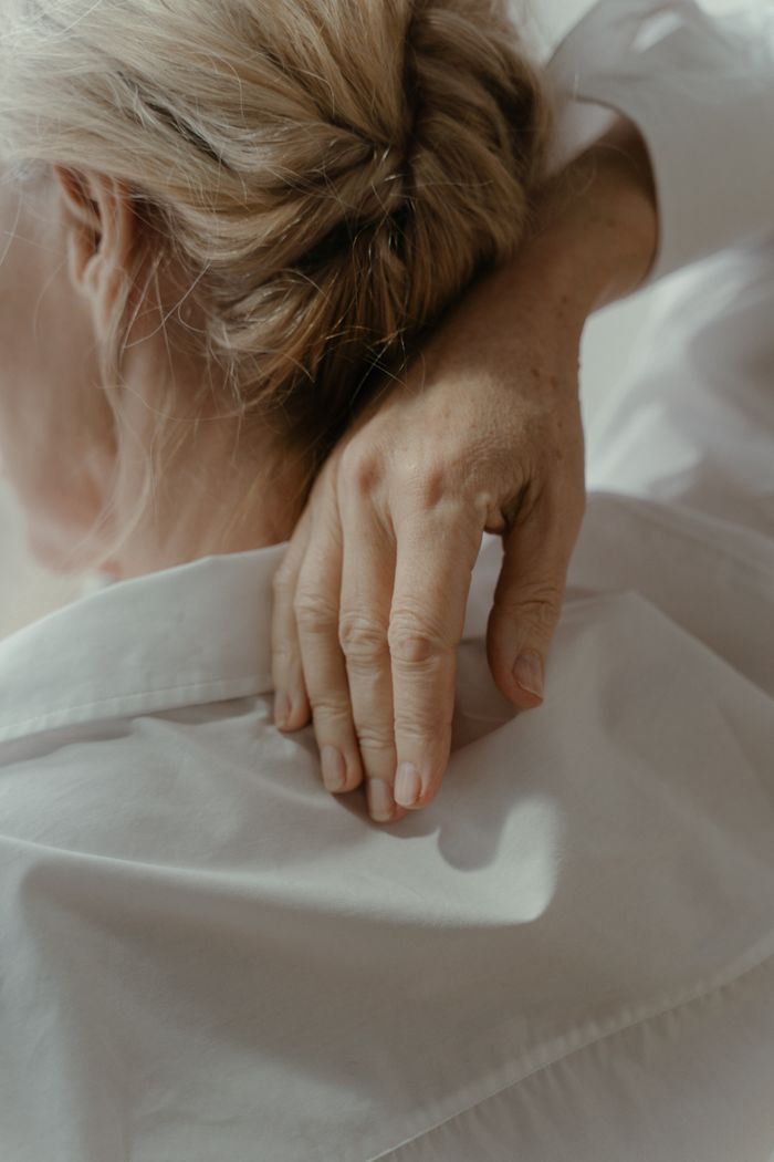 A peaceful close-up image of a woman touching her neck, wearing a white shirt.